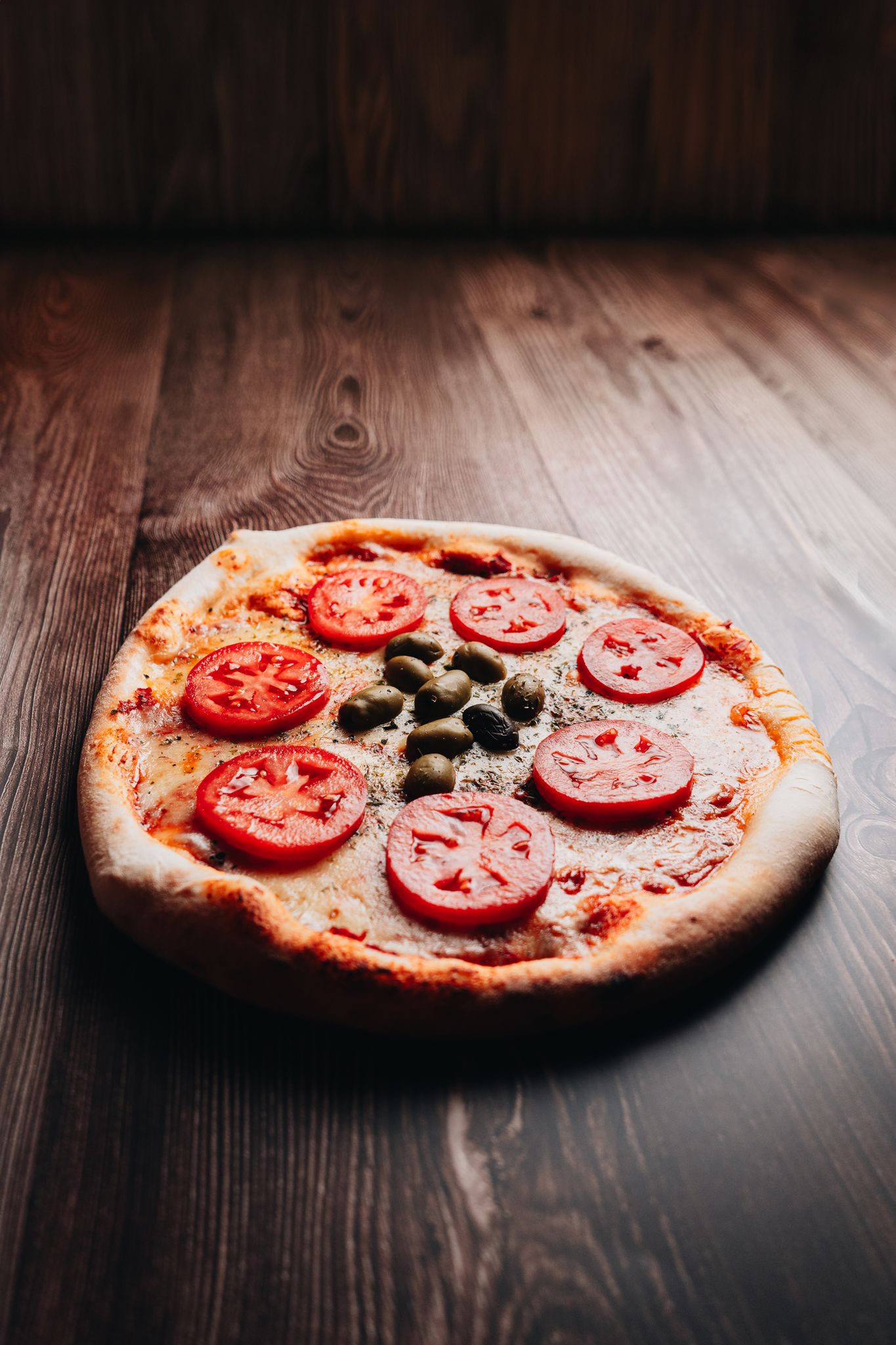 Close-up of a fresh pizza with tomatoes and olives on a wooden table in Mendoza, Argentina.