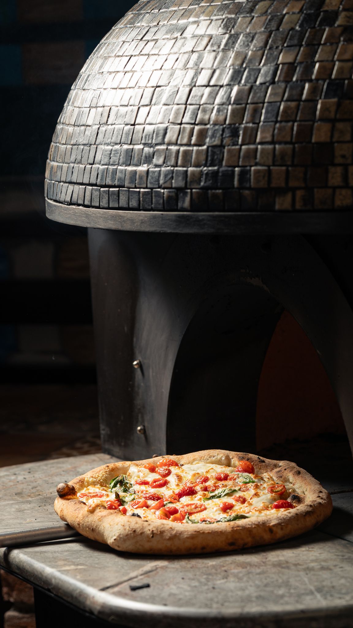 Hot and delicious pizza with tomatoes and basil near a rustic brick oven.